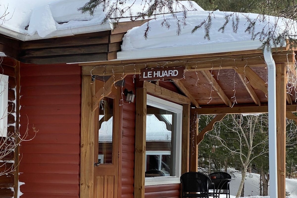 En træhytte med en overdækket veranda og et skilt, der viser "LE HUARD".