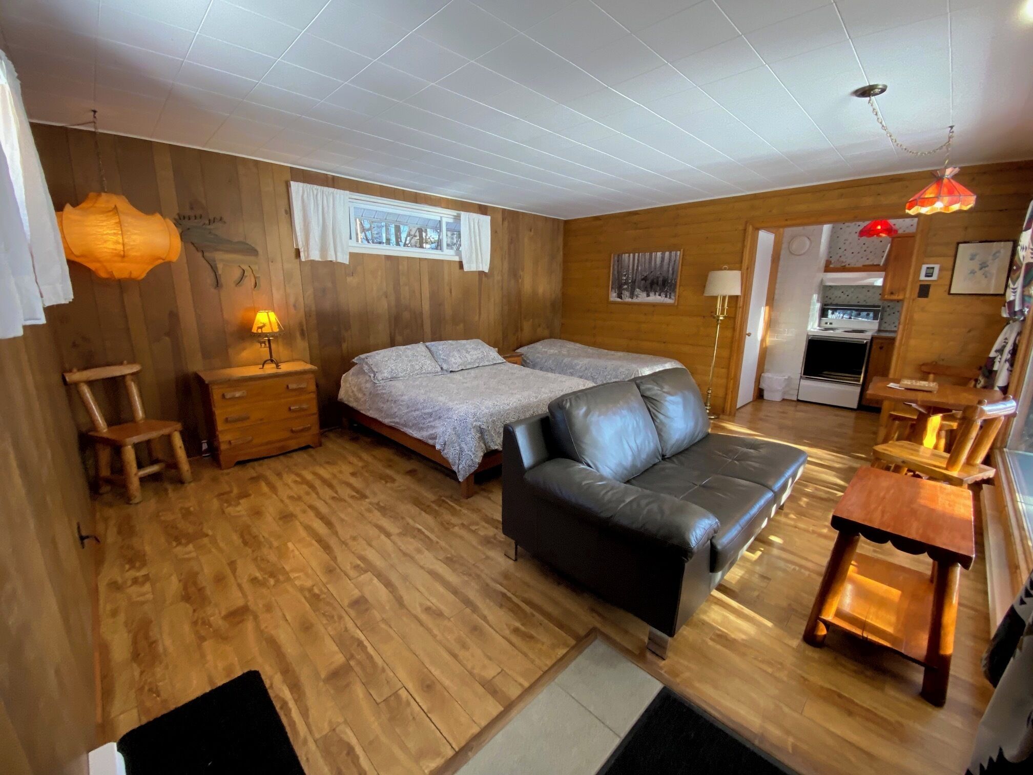 A cozy room with a bed, two bedside tables, a sofa, a small wooden table, and a kitchen area.
