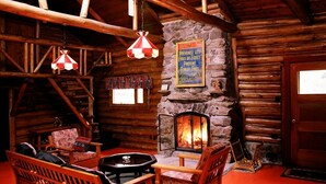 A cozy log cabin interior with a stone fireplace, wooden furniture, and a fire burning. - Kan-à-Mouche Pourvoirie Auberge et Chalets (Saint-Michel-des-Saints)