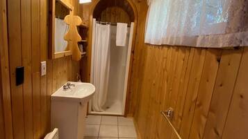 Ein schmales Badezimmer aus Holz mit Waschbecken, Spiegel und Dusche.