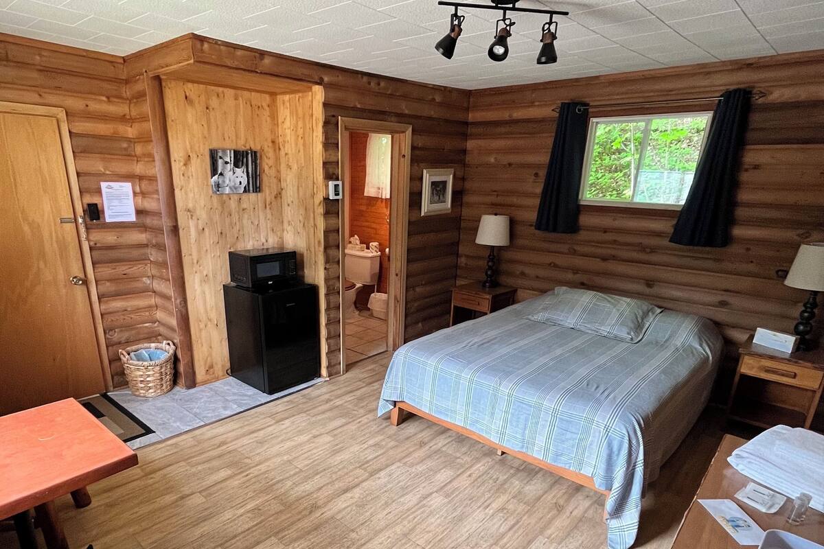 Et hyggeligt værelse i sommerhusstil med seng, skrivebord, stol, lille bord, pejs og et vindue.