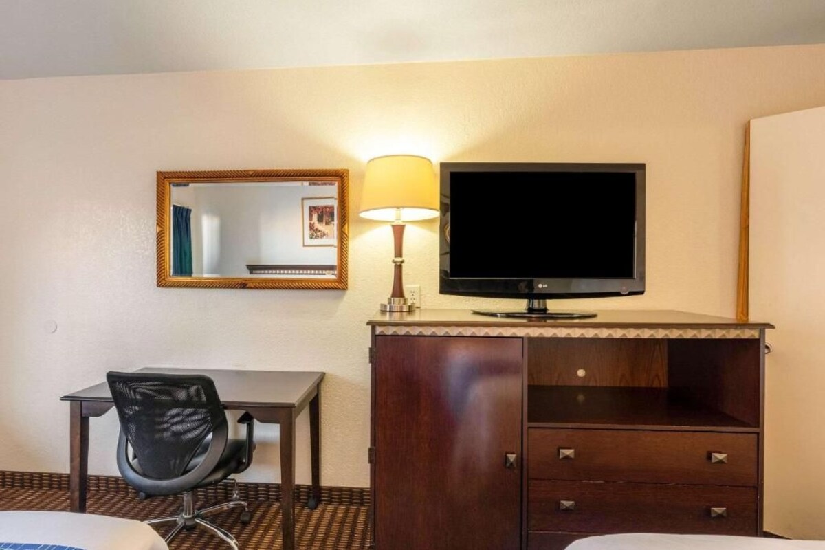 A hotel room with a bed, a desk with a chair, a TV, a mirror, and a cabinet.