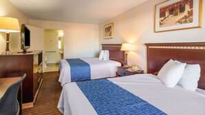 Habitación de hotel con dos camas, un escritorio, una silla, un televisor y un baño visible a través de una puerta abierta.