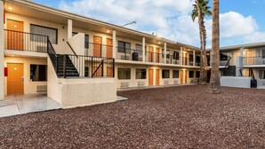Un motel de varios pisos con un patio de grava, escaleras exteriores y palmeras.