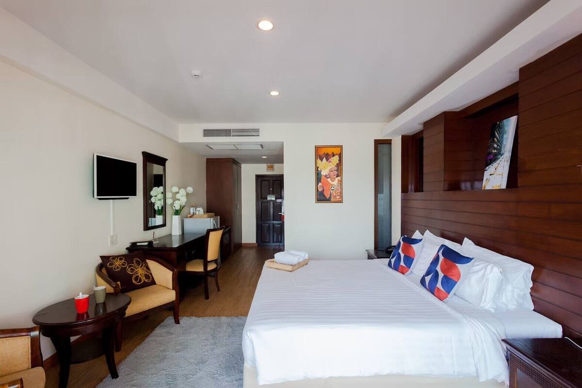 A hotel room with a large bed, a desk with a chair, a television, and a painting on the wall.
