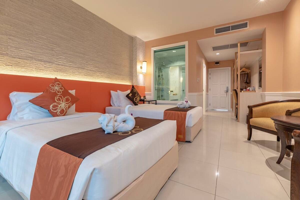 A hotel room with two beds, a sitting area with a table, and a bathroom visible through an open door.