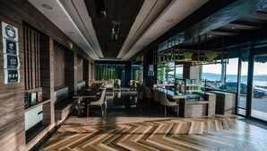 A modern restaurant with a long counter, wooden flooring, and large windows offering a view of the sea. - Seaside Jomtien Beach (Pattaya)
