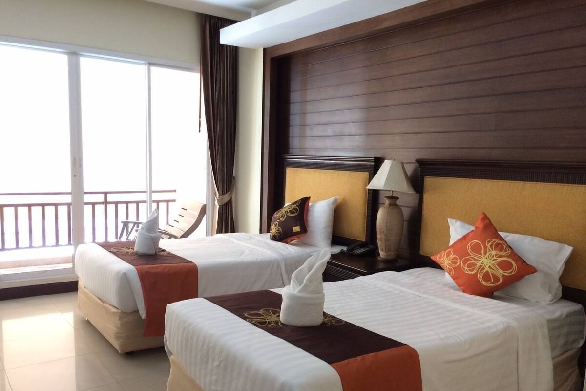 A hotel room with two beds, a balcony, a wooden headboard, a nightstand with a lamp, and a telephone.