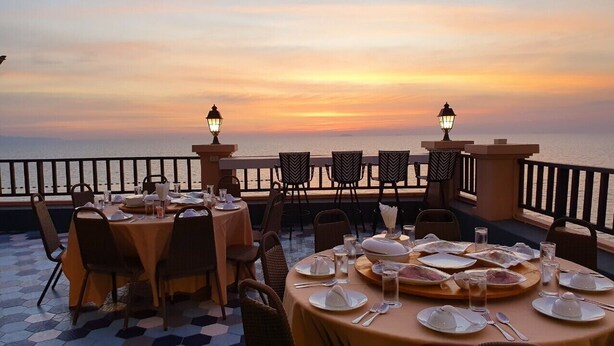 A restaurant with tables set for dining, overlooking a body of water during sunset. - Seaside Jomtien Beach (Pattaya)