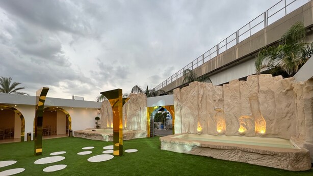 Un espacio exterior moderno con césped artificial, una cascada de rocas y un puente.