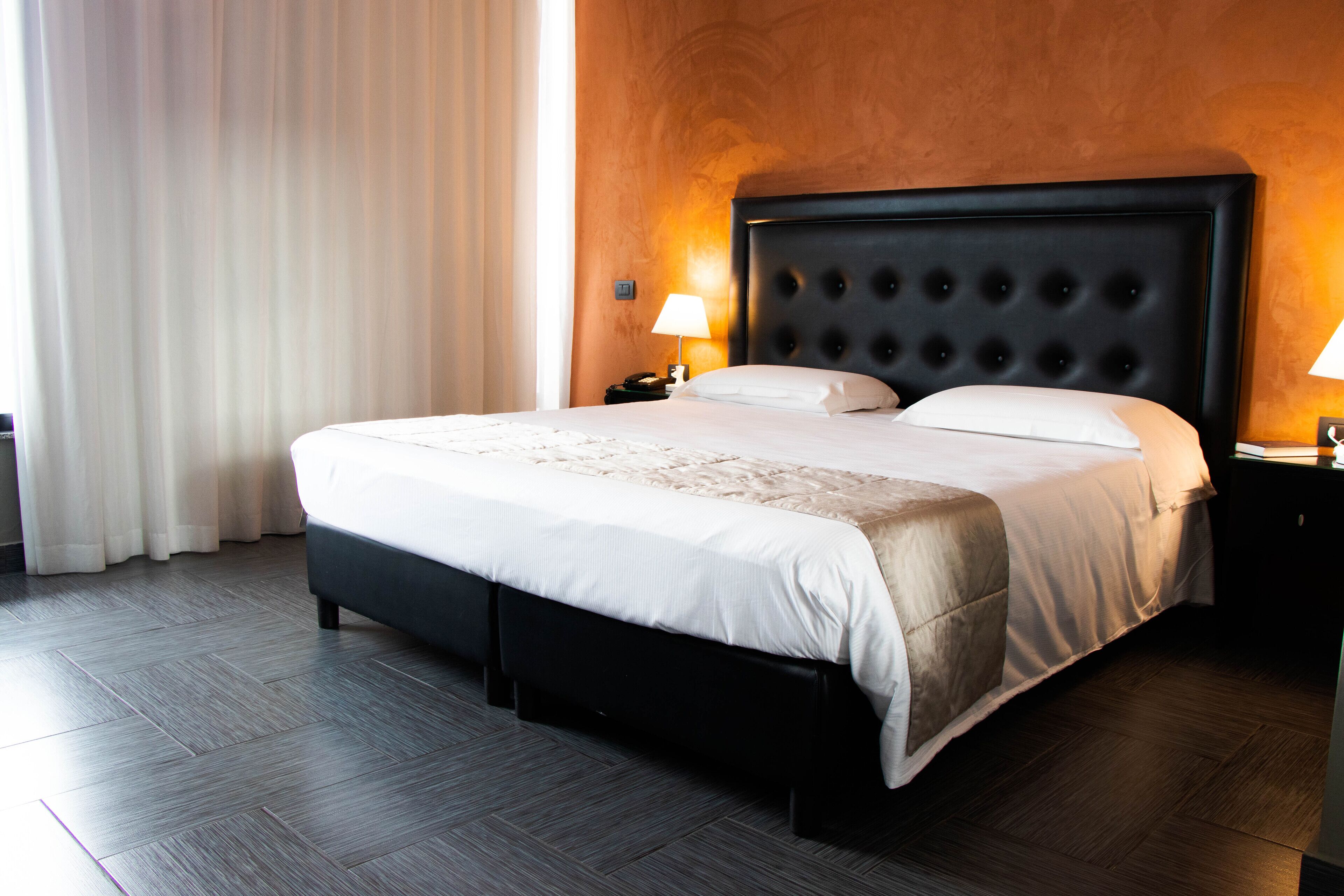 Una habitación de hotel con una cama grande, un cabecero oscuro y una mesita de noche con una lámpara.
