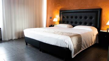 Una habitación de hotel con una cama grande, un cabecero oscuro y una mesita de noche con una lámpara.