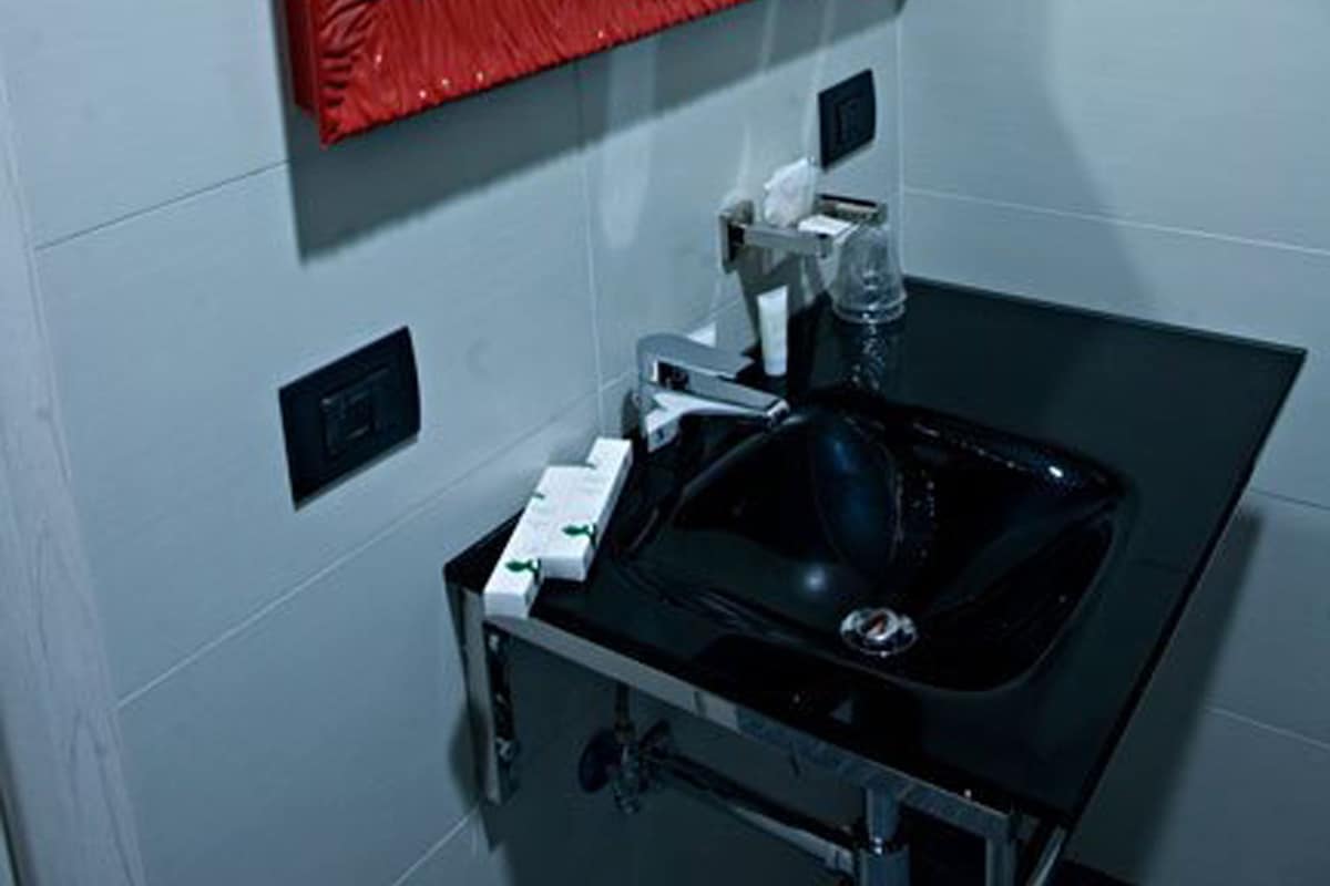 A bathroom with a black sink, a red-framed mirror, and white tiled walls.