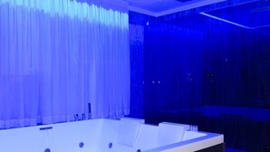 Un baño moderno con una bañera grande, piso de madera e iluminación ambiental azul.