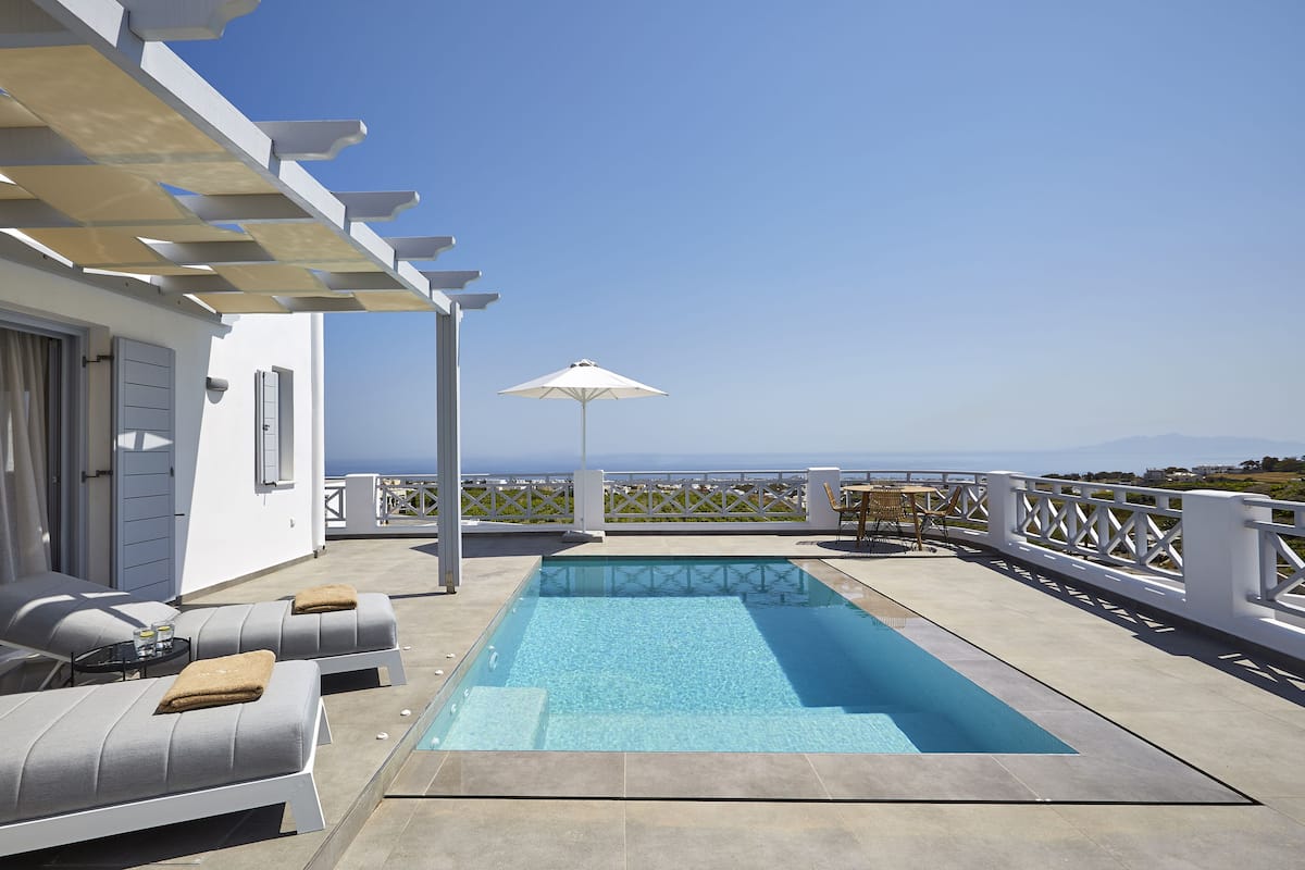 A rooftop pool area with a view of the sea, outdoor seating, and a pergola.