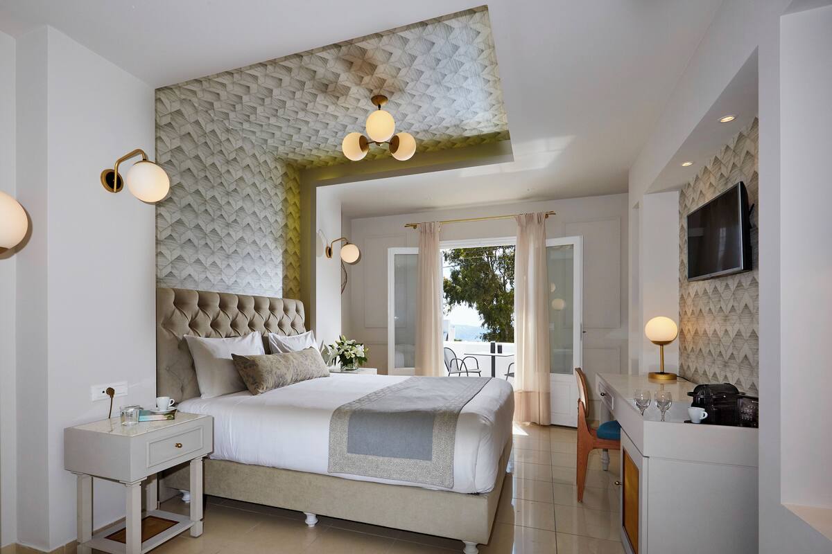A modern bedroom with a tufted headboard, a bedside table with a lamp, and a large window with curtains.