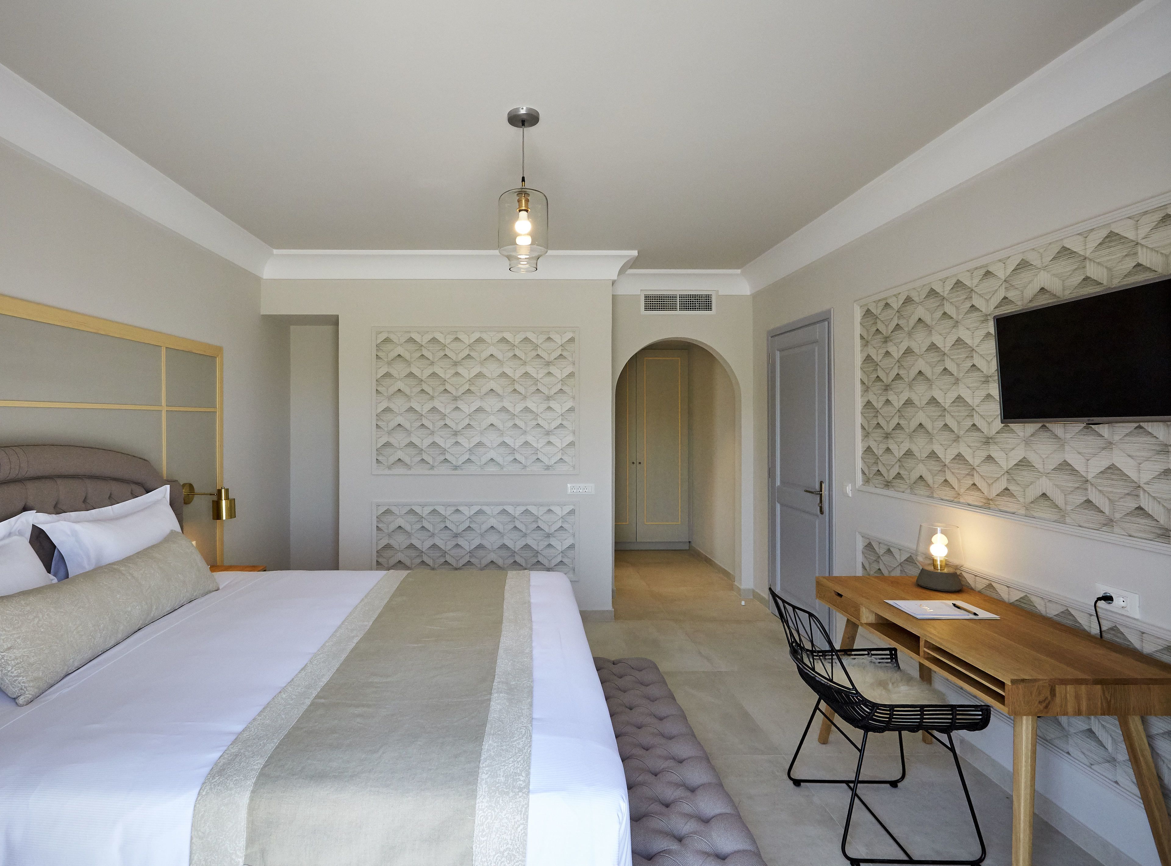 A modern hotel room with a bed, bedside table, desk, and chair.