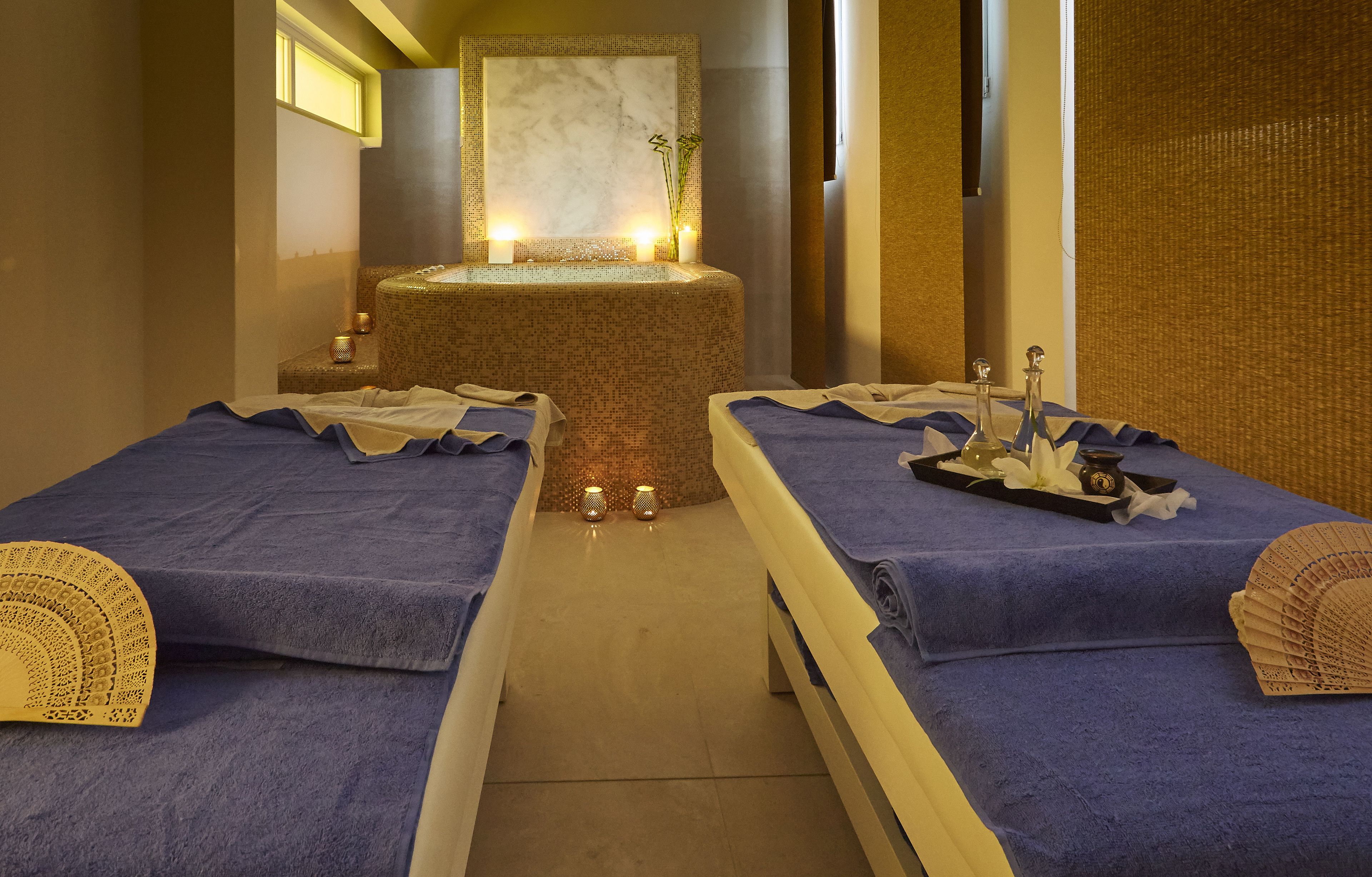 Um quarto de spa com duas camas, uma pia de mármore central e velas.