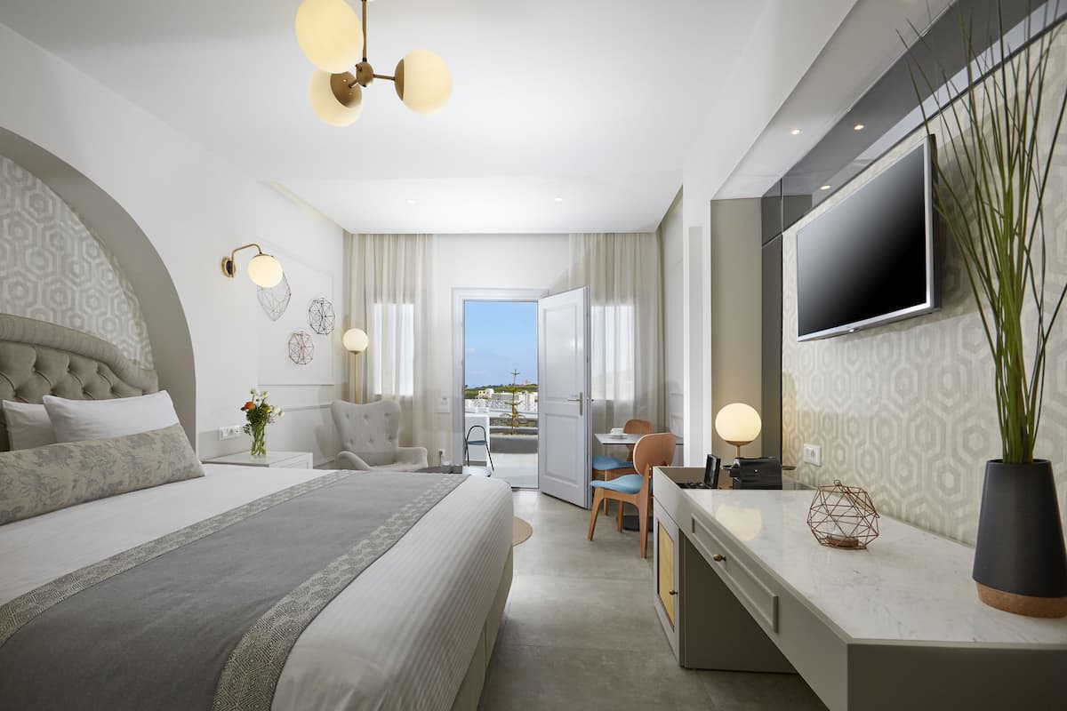 A modern hotel room with a large bed, a desk, a TV, and a balcony with a view.