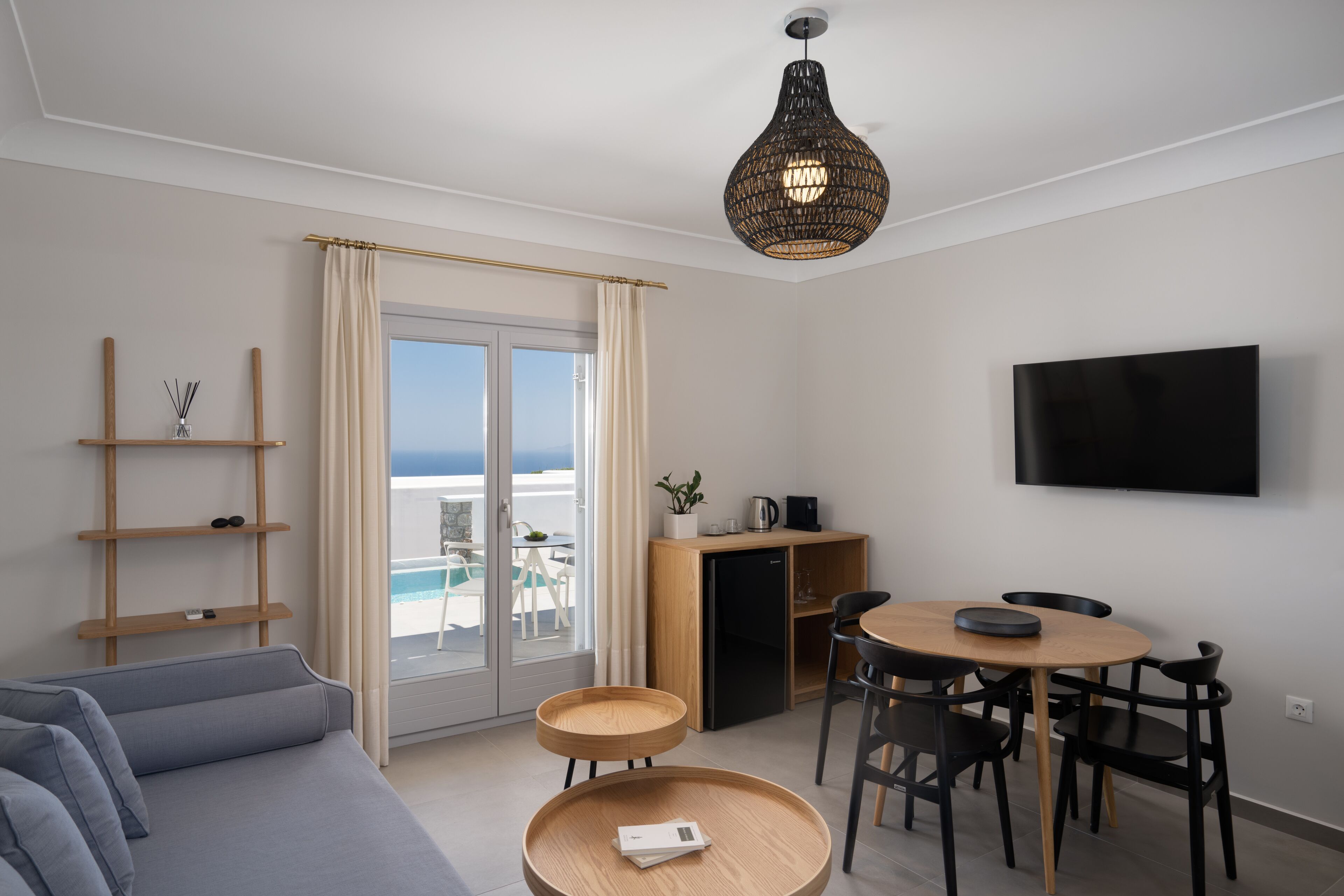 Una sala de estar moderna con un sofá, una mesa de comedor con sillas, un televisor montado en la pared y un balcón con vista al mar.