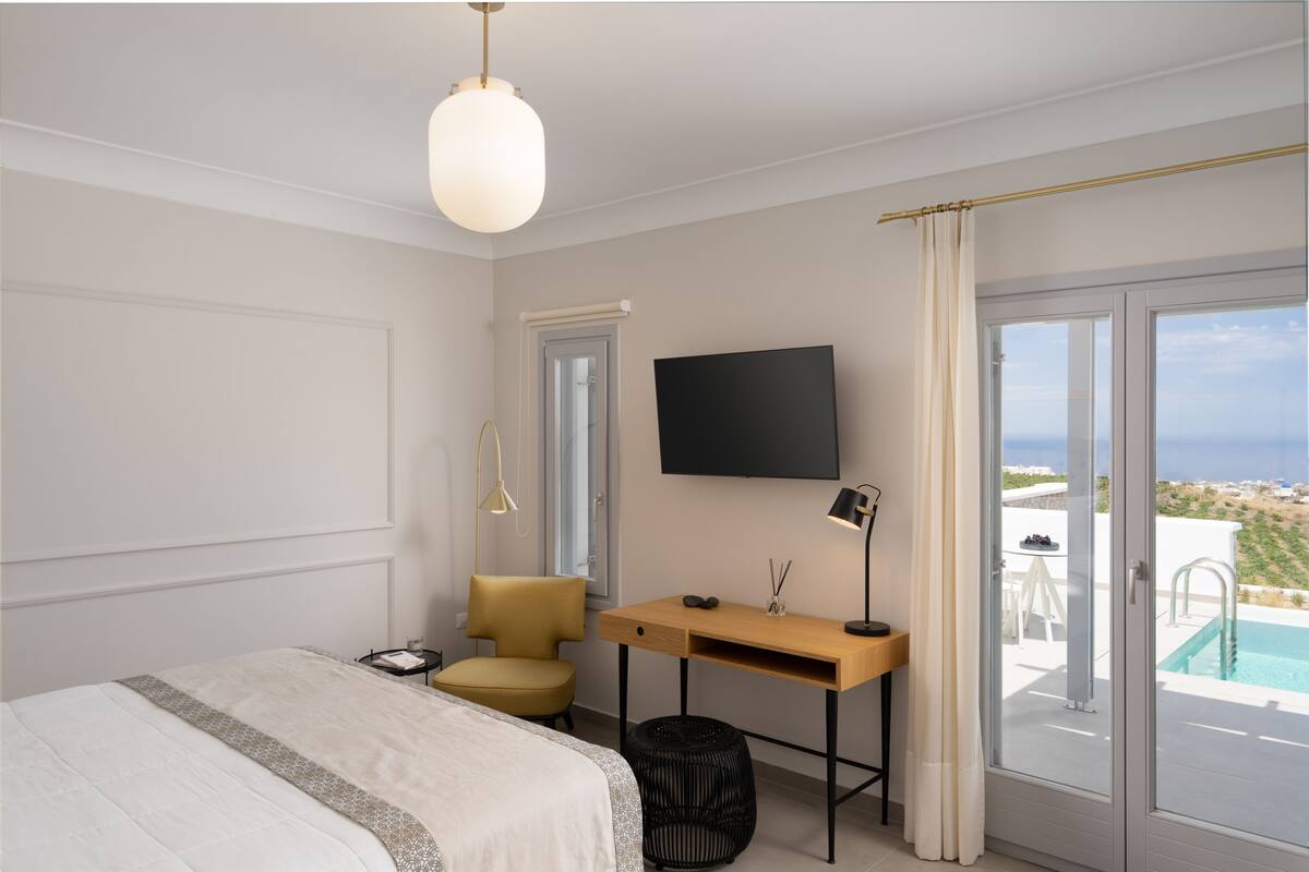 A bedroom with a bed, a desk, a chair, a TV, and a view of a swimming pool.