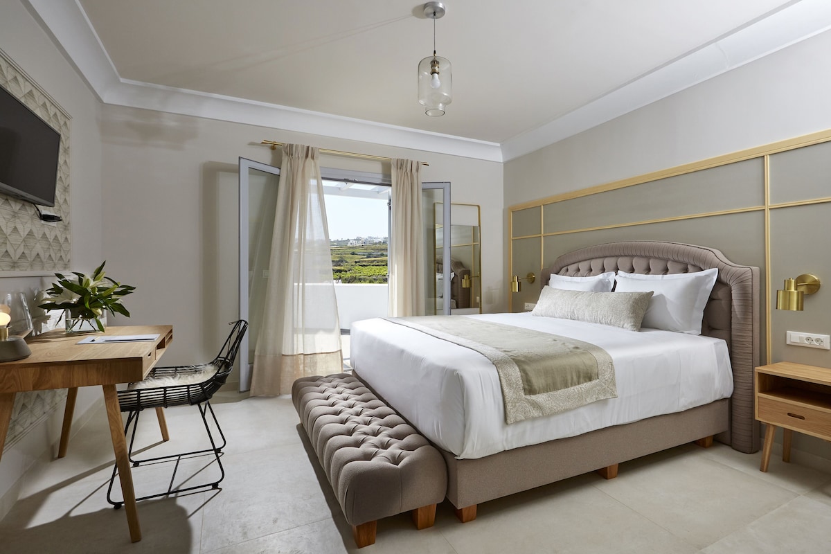 A bedroom with a large bed, a desk, a chair, a bench, and a bedside table.