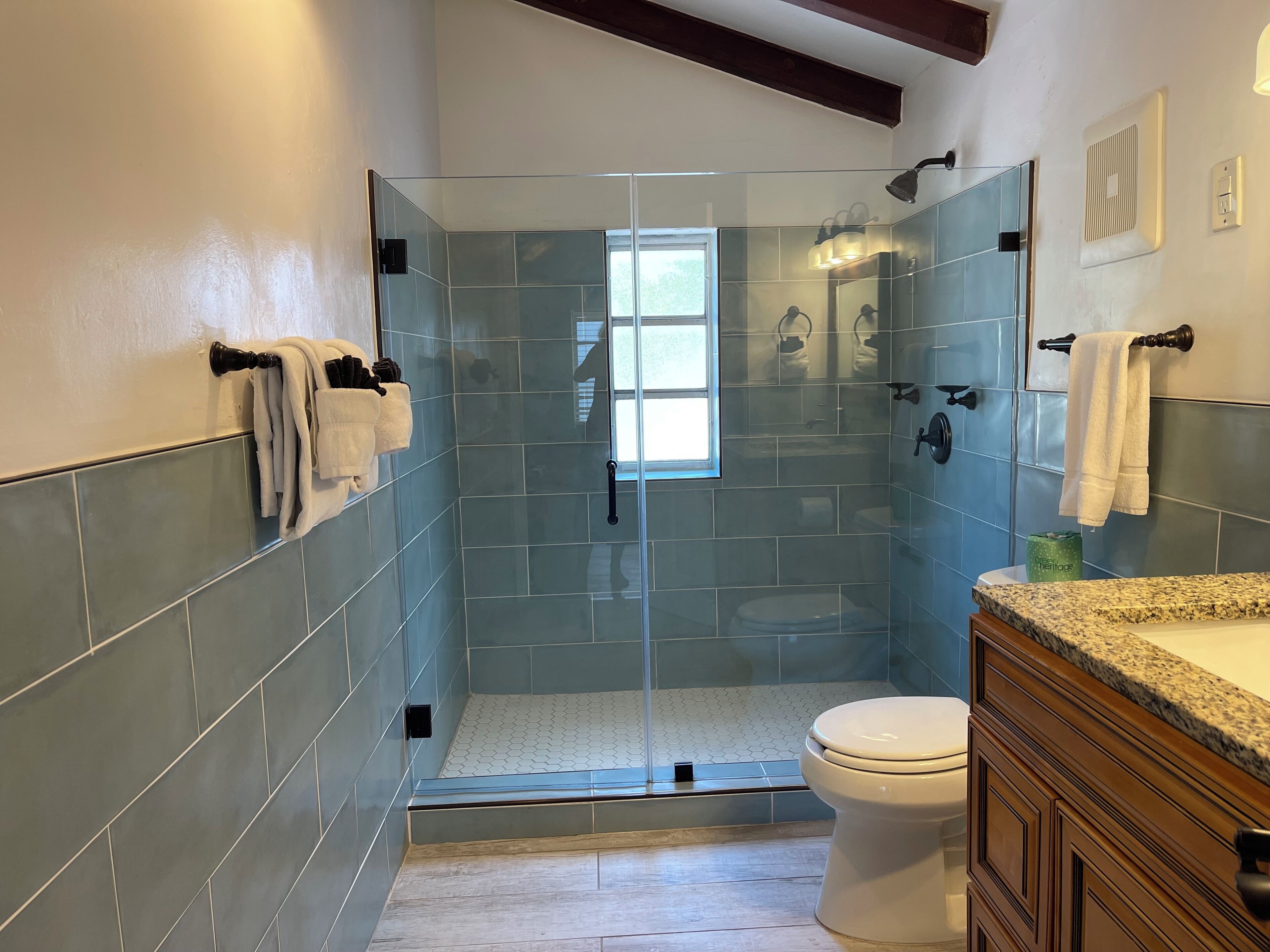 A modern bathroom with a glass-enclosed shower, a white toilet, and a granite countertop.