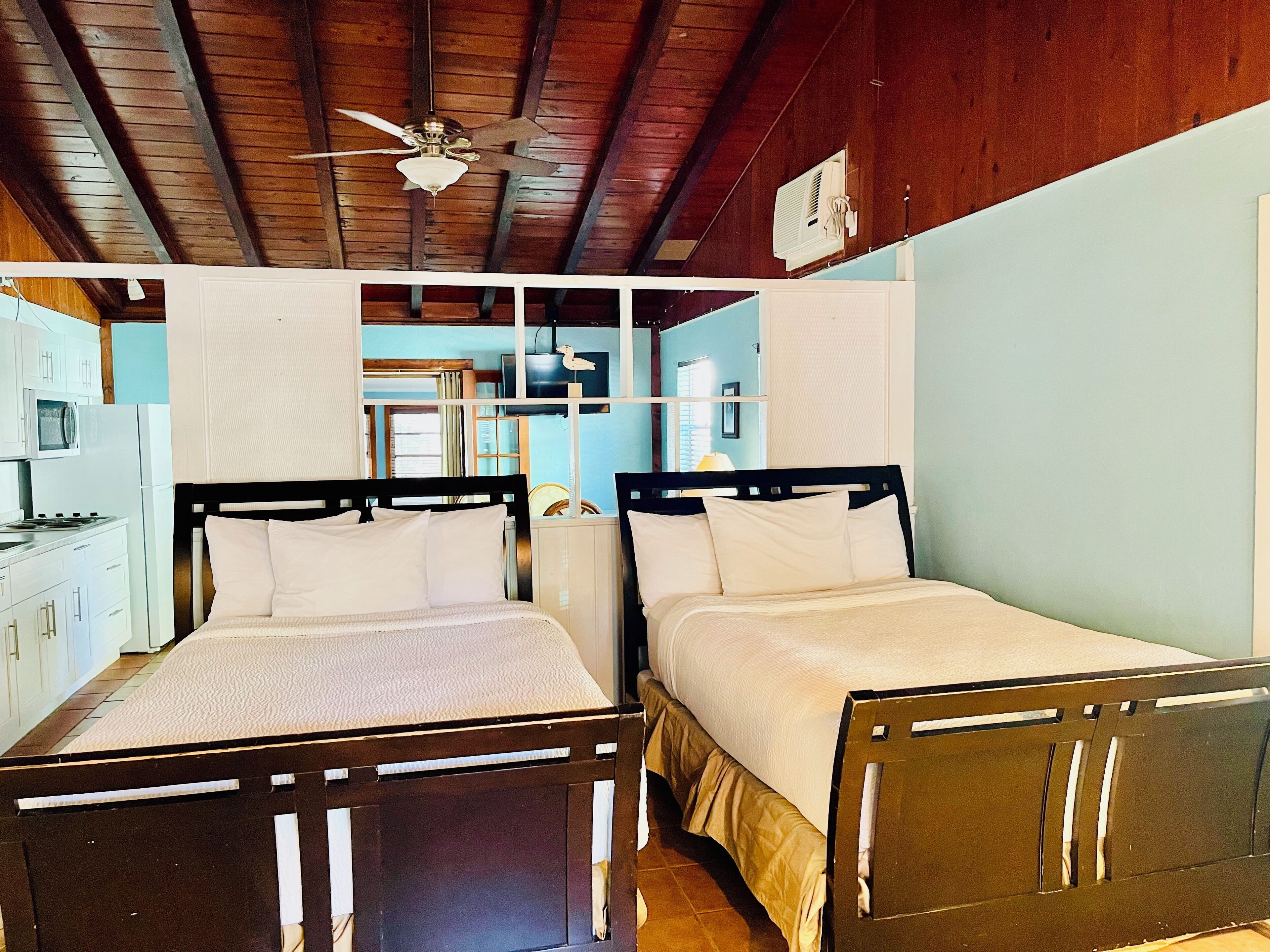 Un dormitorio con dos camas, cabeceros de madera, ventilador de techo y una kitchenette con microondas y refrigerador.