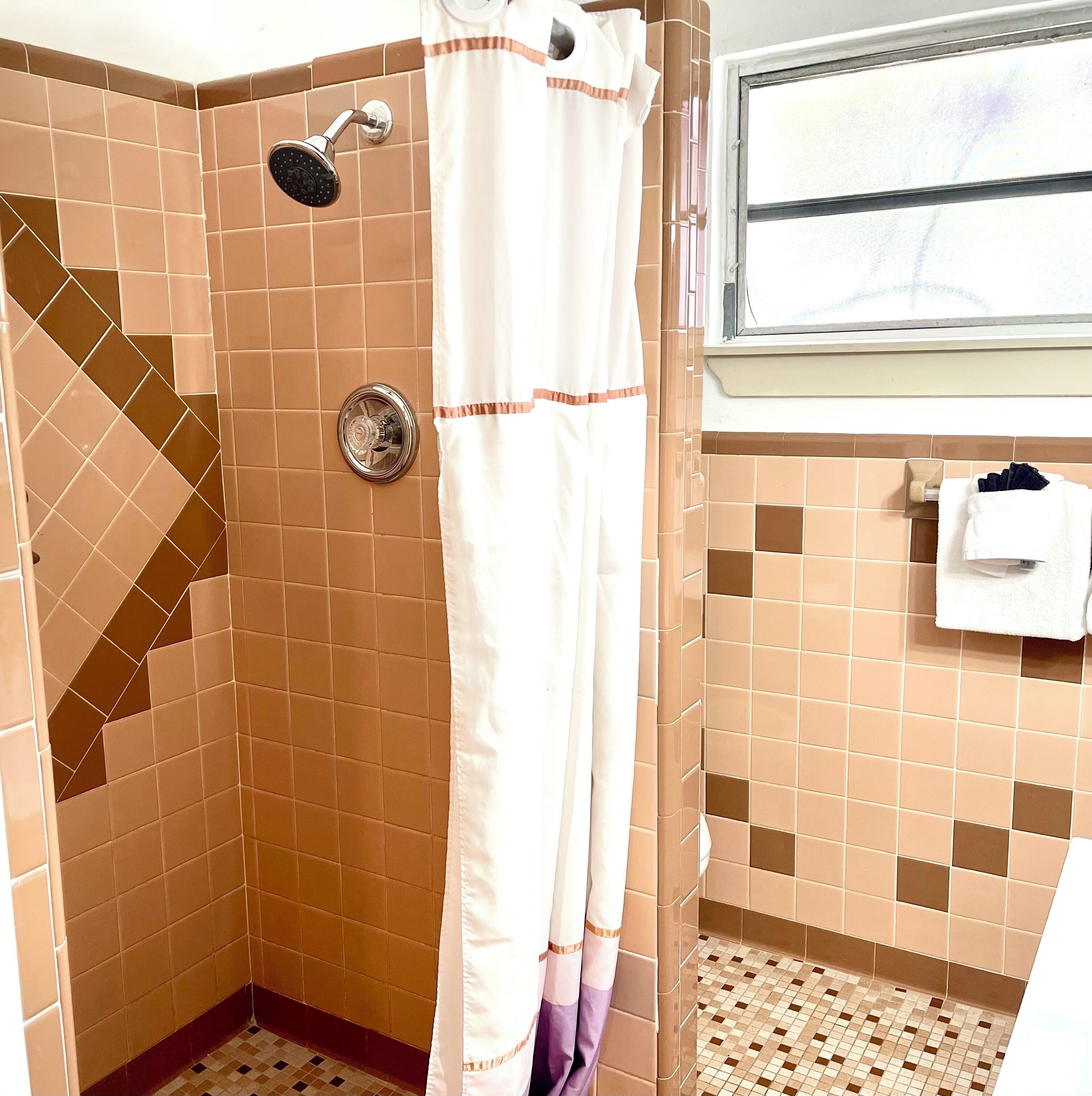 A shower with a handheld showerhead, a curtain, and a towel rack with a towel.