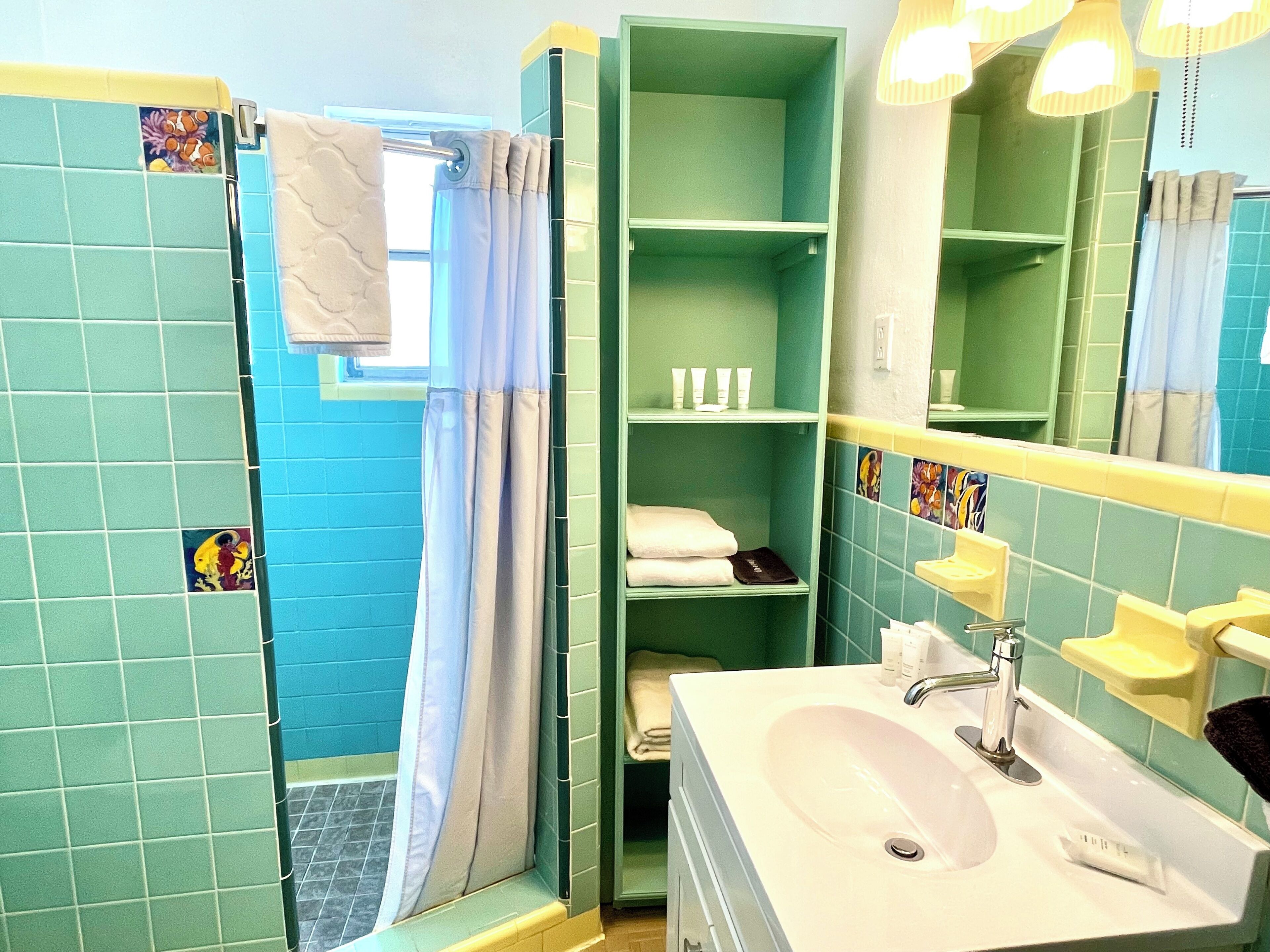 Une salle de bain équipée d’une douche, d’un lavabo et d’étagères où sont rangés les produits de toilette.