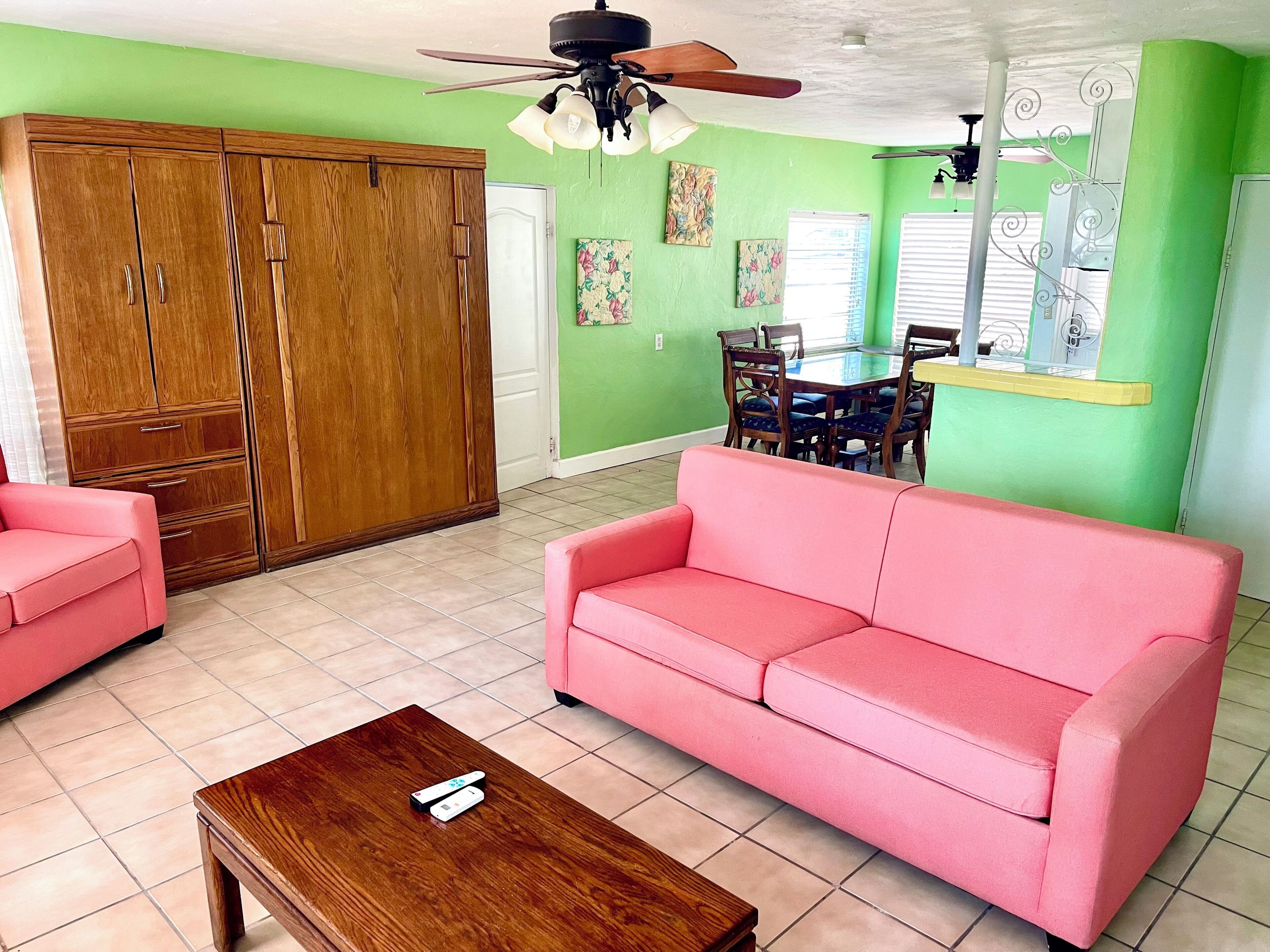 A living room with a wooden wardrobe, a pink sofa, a wooden coffee table, and a ceiling fan.