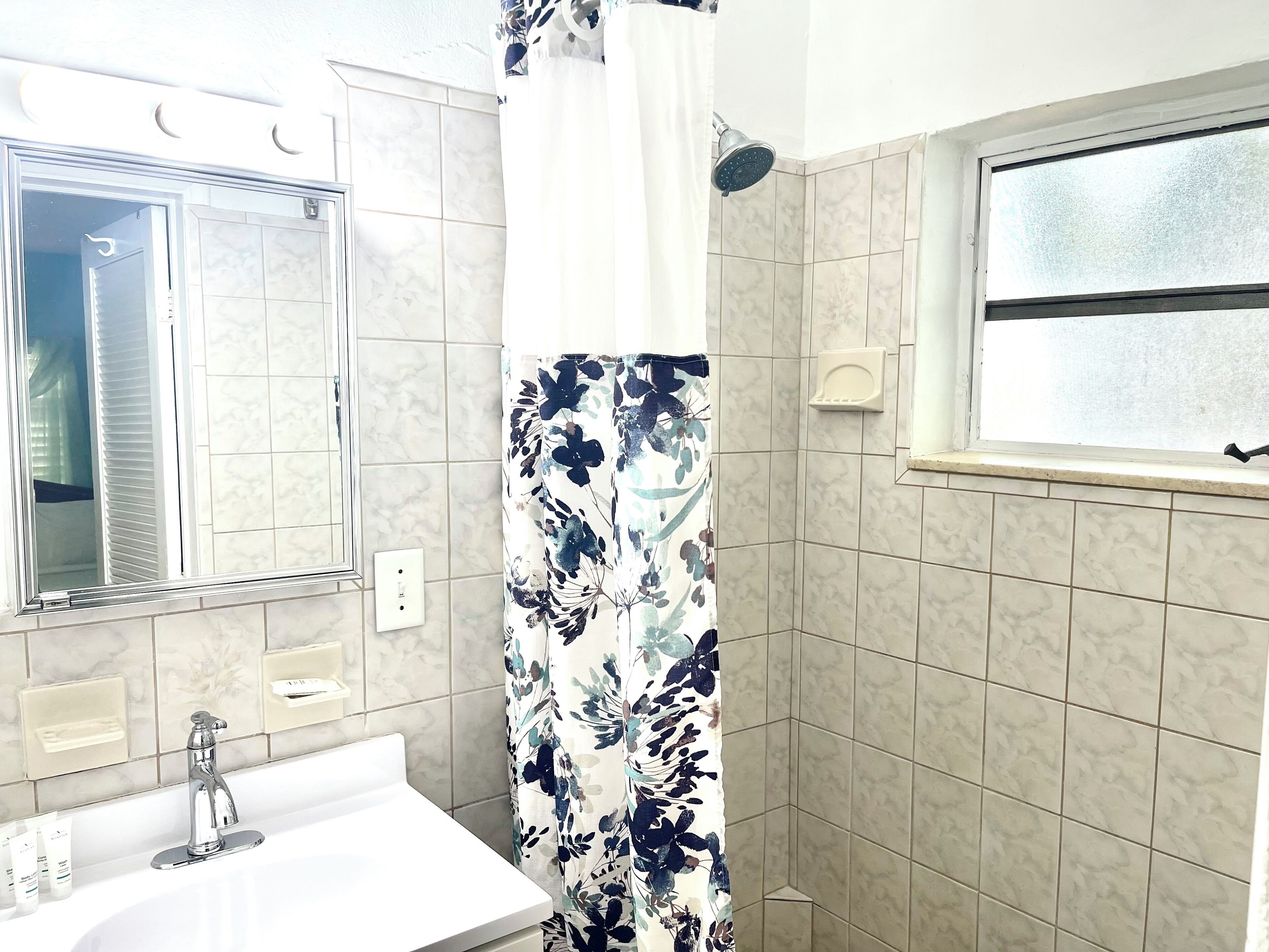 A bathroom with a white sink, a mirror, a shower with a floral curtain, and beige tiled walls.