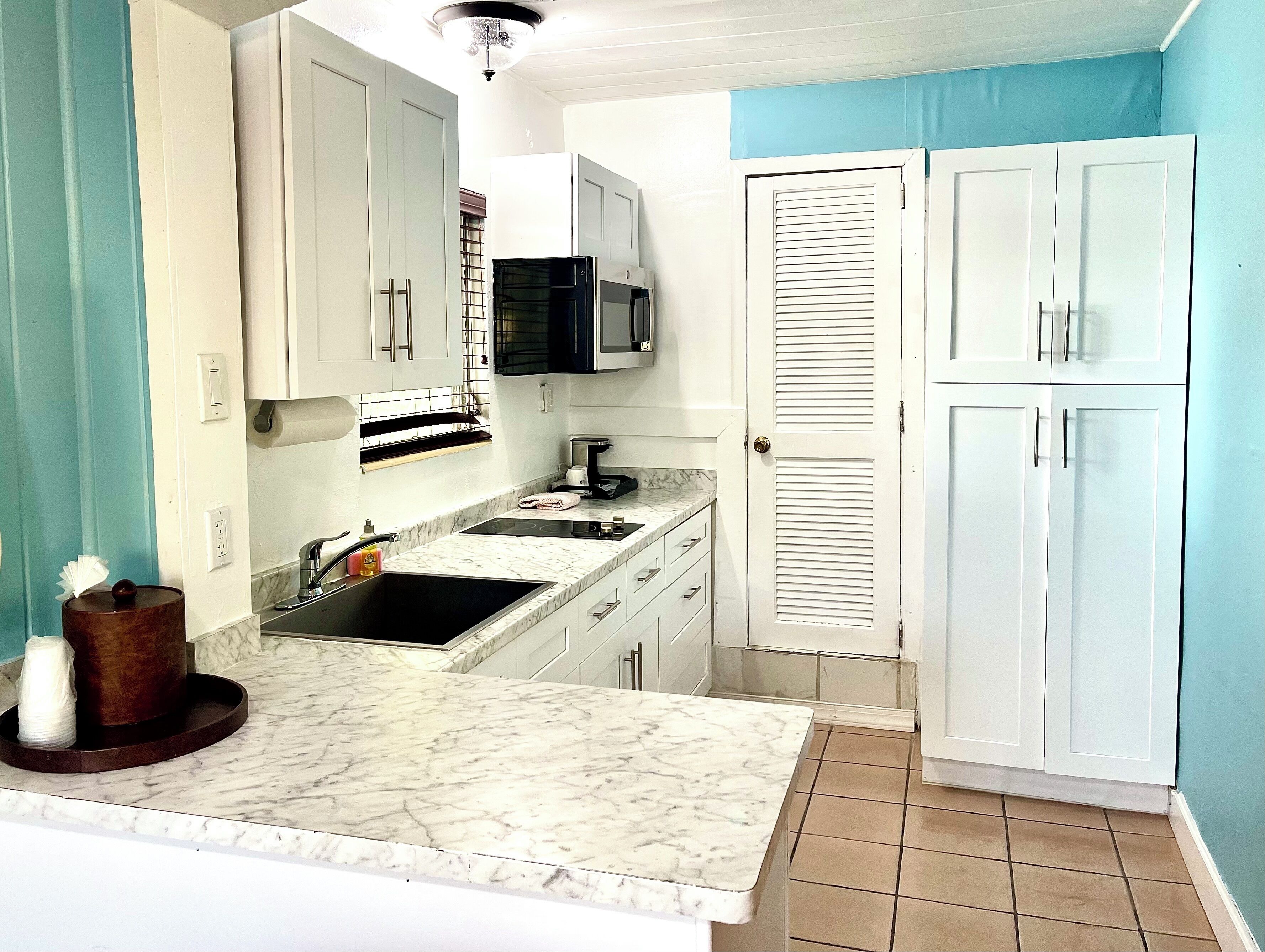A compact kitchen with white cabinets, a black microwave, and a sink.