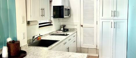 A compact kitchen with white cabinets, a black microwave, and a sink.