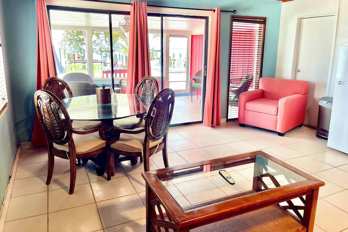 Un coin repas avec une table et des chaises en verre, un canapé rouge et une porte-fenêtre coulissante donnant sur un espace extérieur.
