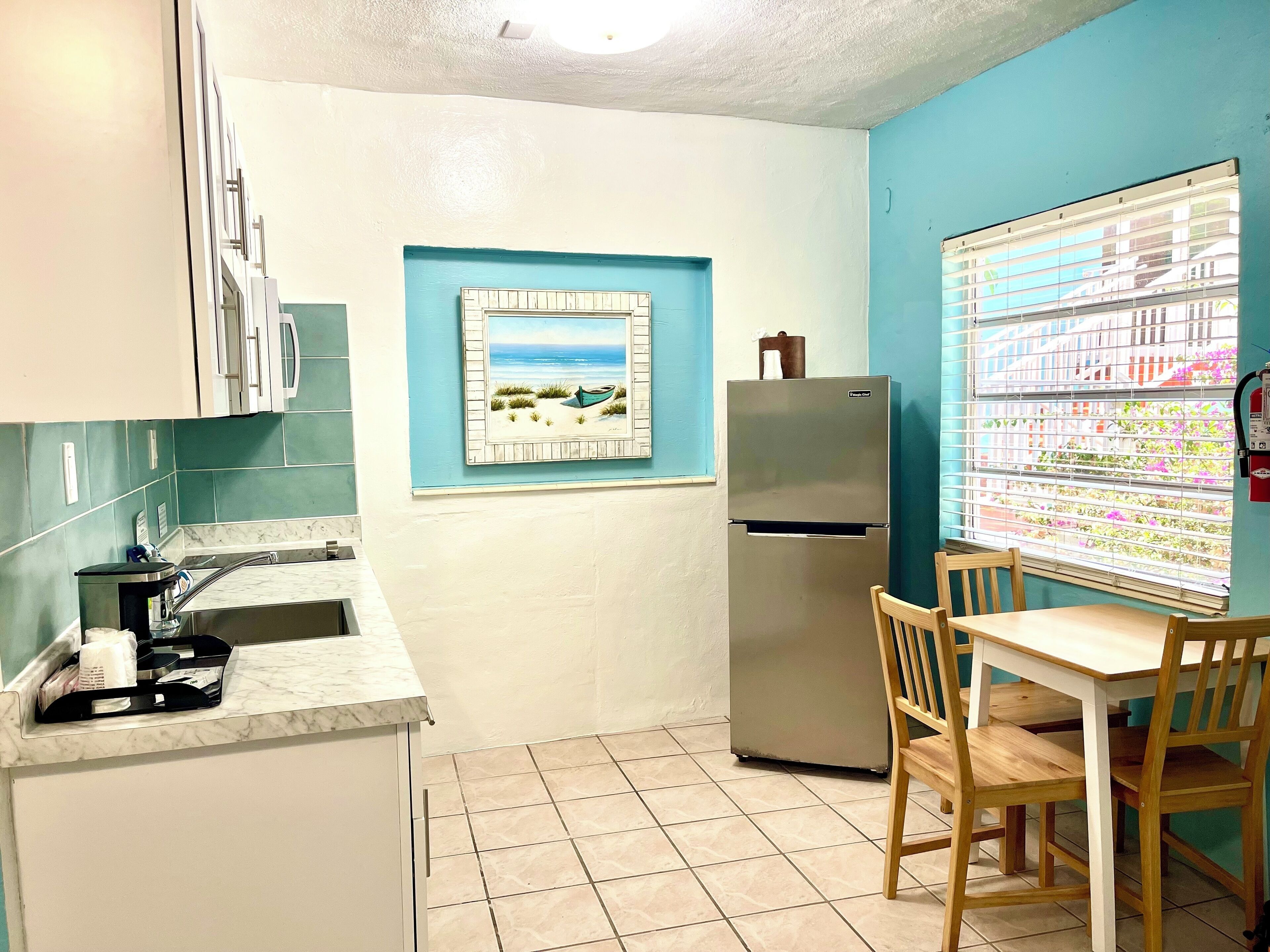 A compact kitchen with a refrigerator, a sink, and a dining area with a table and chairs.