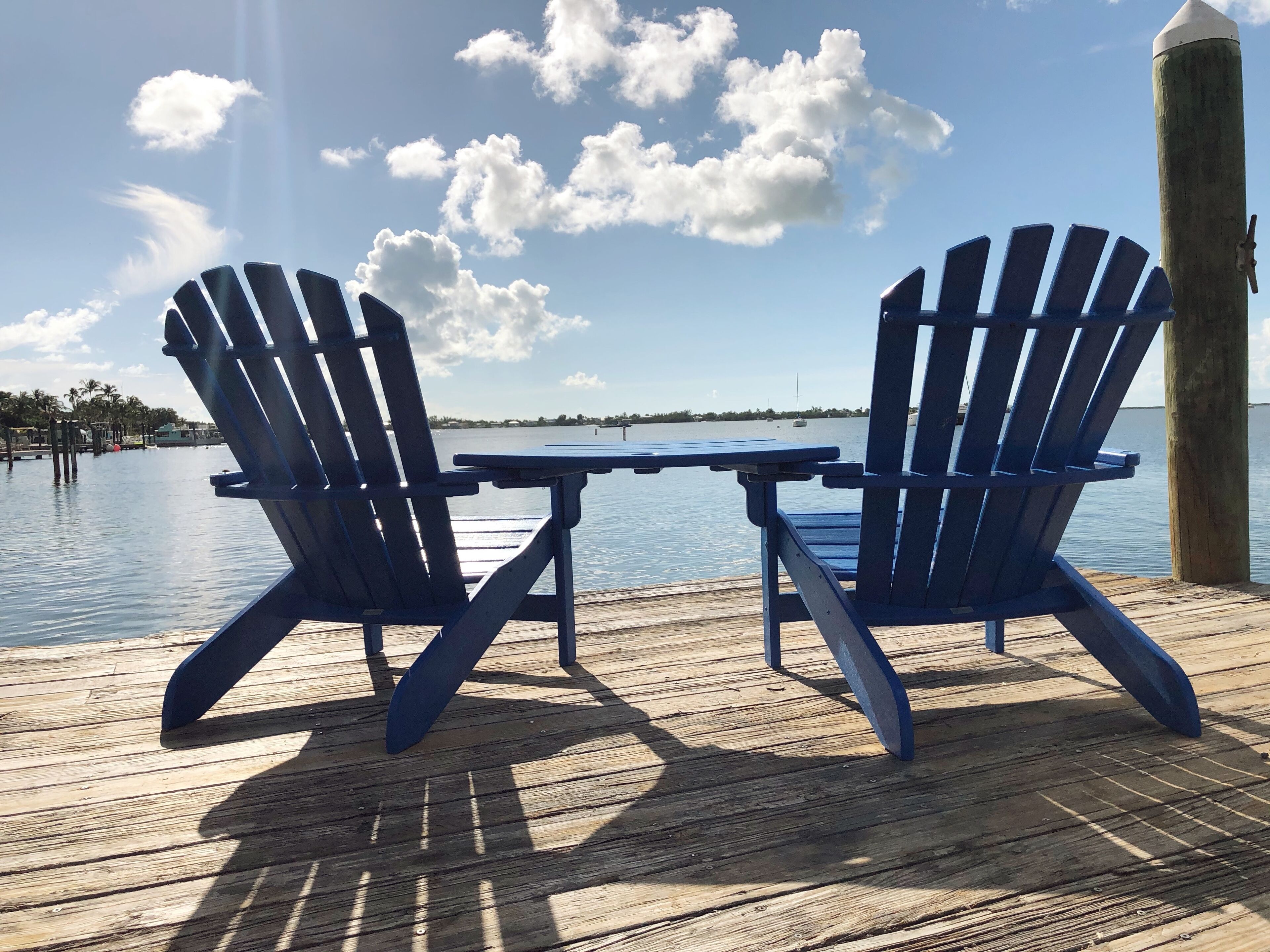 Dos sillas Adirondack azules en una terraza de madera con vista a un agua tranquila y tierra distante.