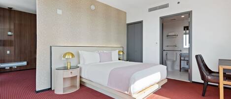 Una habitación de hotel moderna con una cama grande, mesitas de noche, un escritorio y un baño visible a través de una puerta abierta.