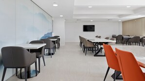 A modern conference room with white tables and chairs, a mounted TV, and a mural on the wall. - The Parc Hotel (Flushing)