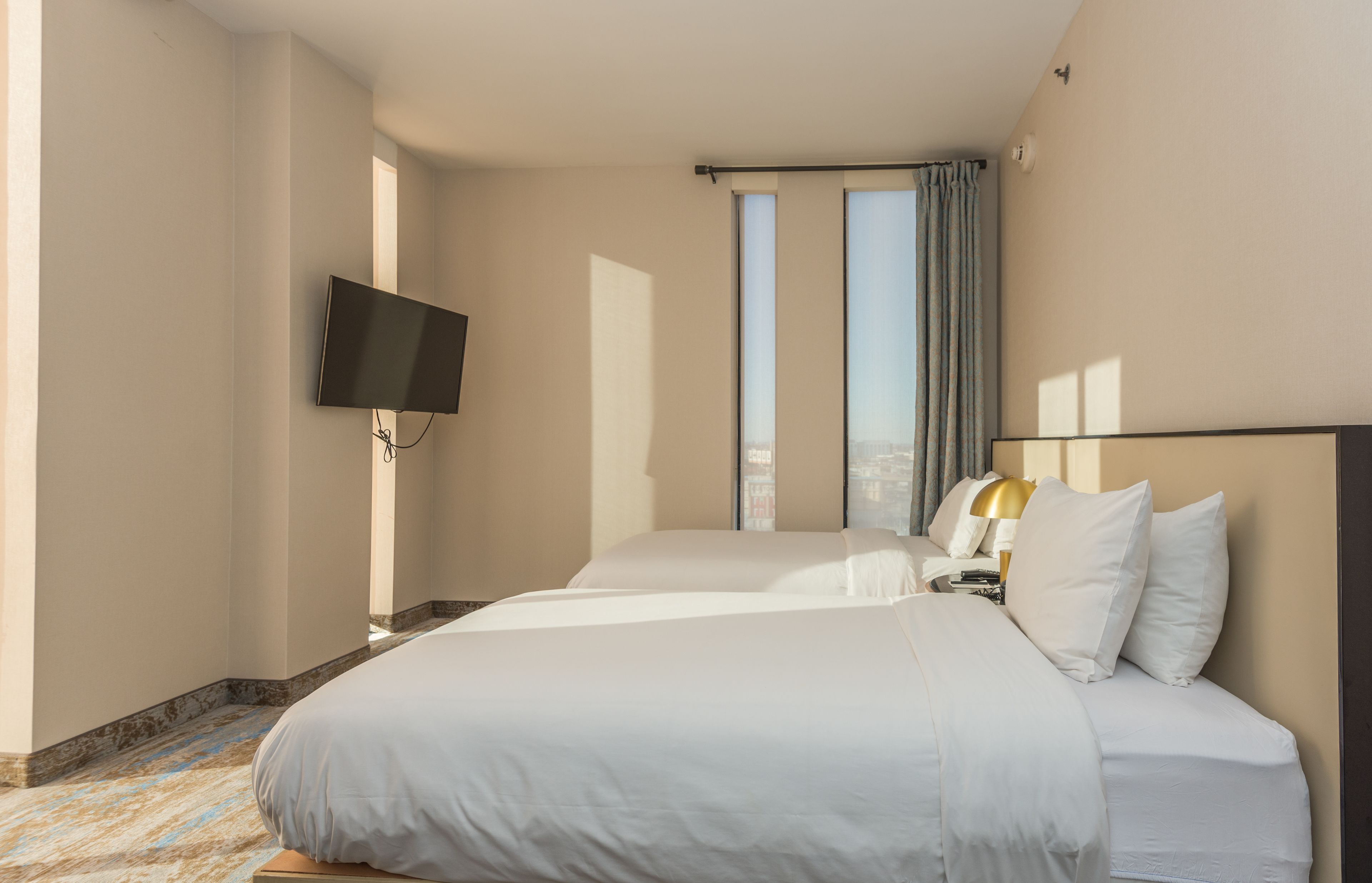 Habitación de hotel con dos camas, un televisor de pantalla plana montado en la pared y una ventana con cortinas.