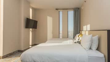 Habitación de hotel con dos camas, un televisor de pantalla plana montado en la pared y una ventana con cortinas.