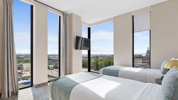 A hotel room with two beds, a TV, and a large window with a city view. - The Parc Hotel (Flushing)