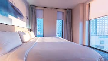 A hotel room with a large bed, a view of a cityscape through the window, and a painting on the wall.