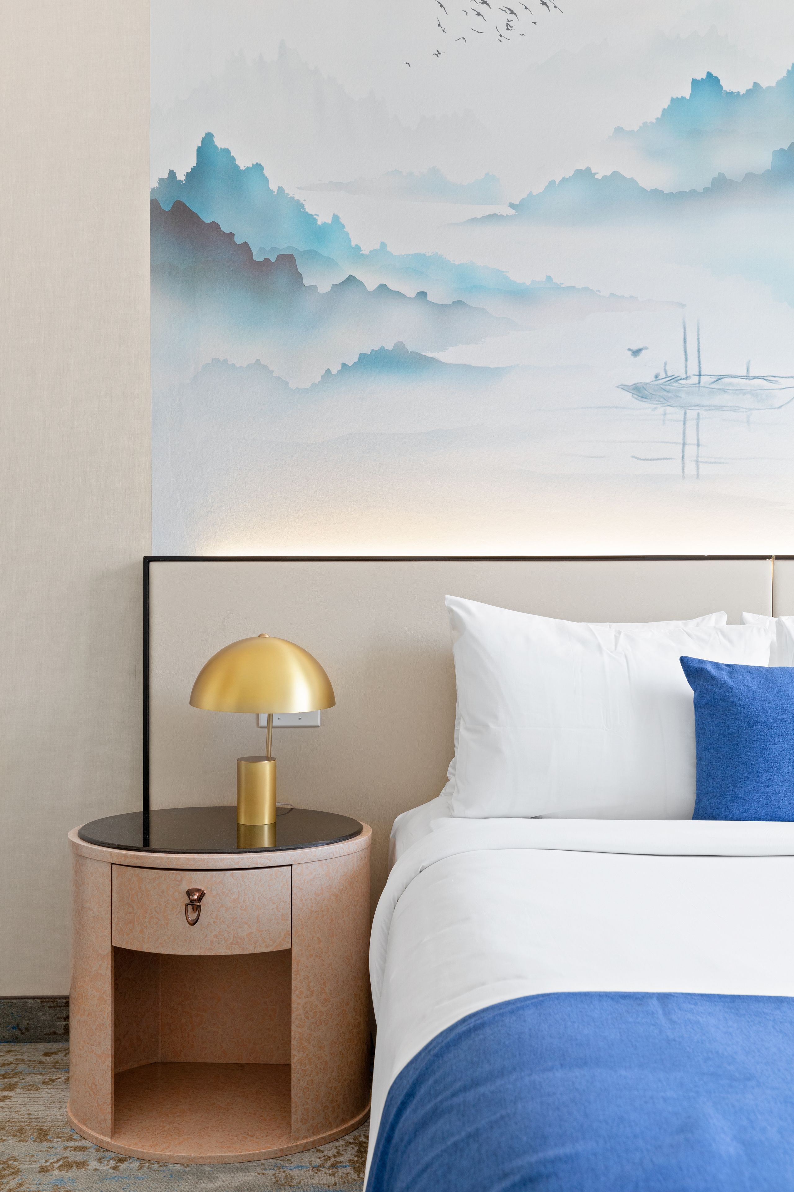 A hotel room with a bed, a bedside table with a lamp, and a wall painting.