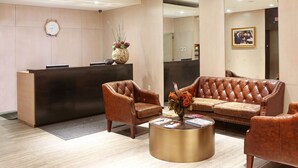 A reception area with a reception desk, leather armchairs, a sofa, and a coffee table with magazines. - The Parc Hotel (Flushing)