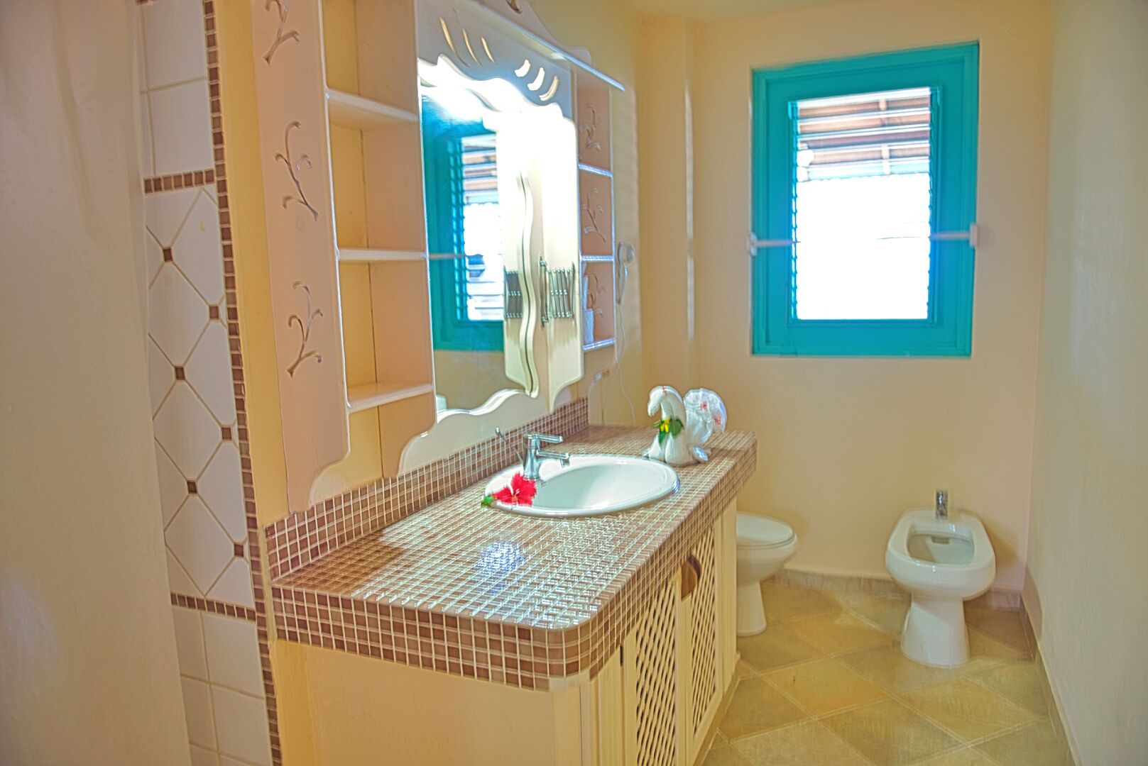 A bathroom with a tiled floor, a sink with a mirror, a toilet, and a window with blinds.