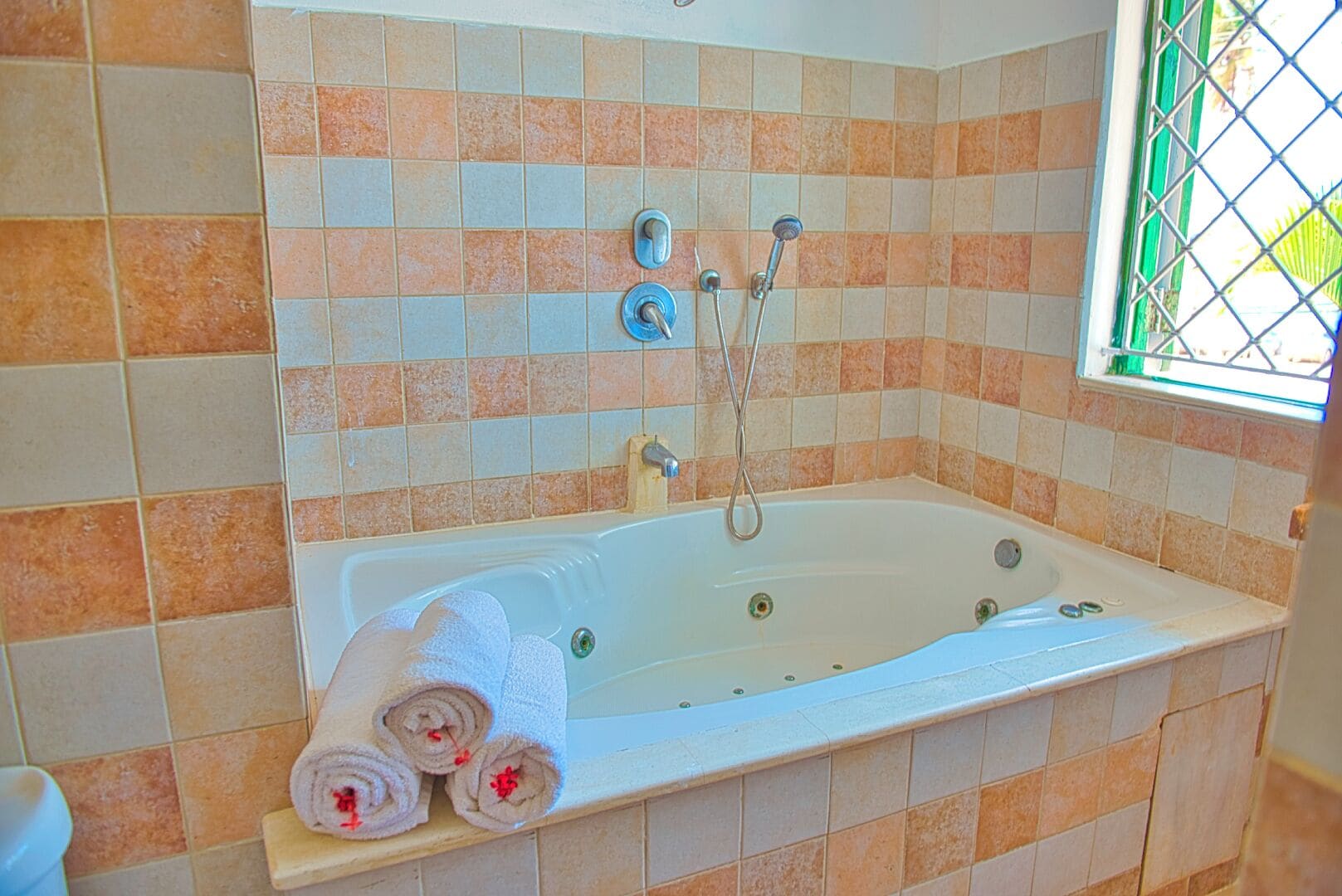 Un baño con bañera, dos toallas enrolladas y una ventana con vistas.