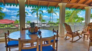 A covered outdoor dining area with a view of the ocean, wooden furniture, and tropical plants. - Villa Chiara Las Terrenas (Las Terrenas)