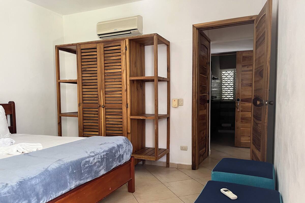 Un dormitorio con un armario de madera, una cama con colchón azul y una mesita con un control remoto.