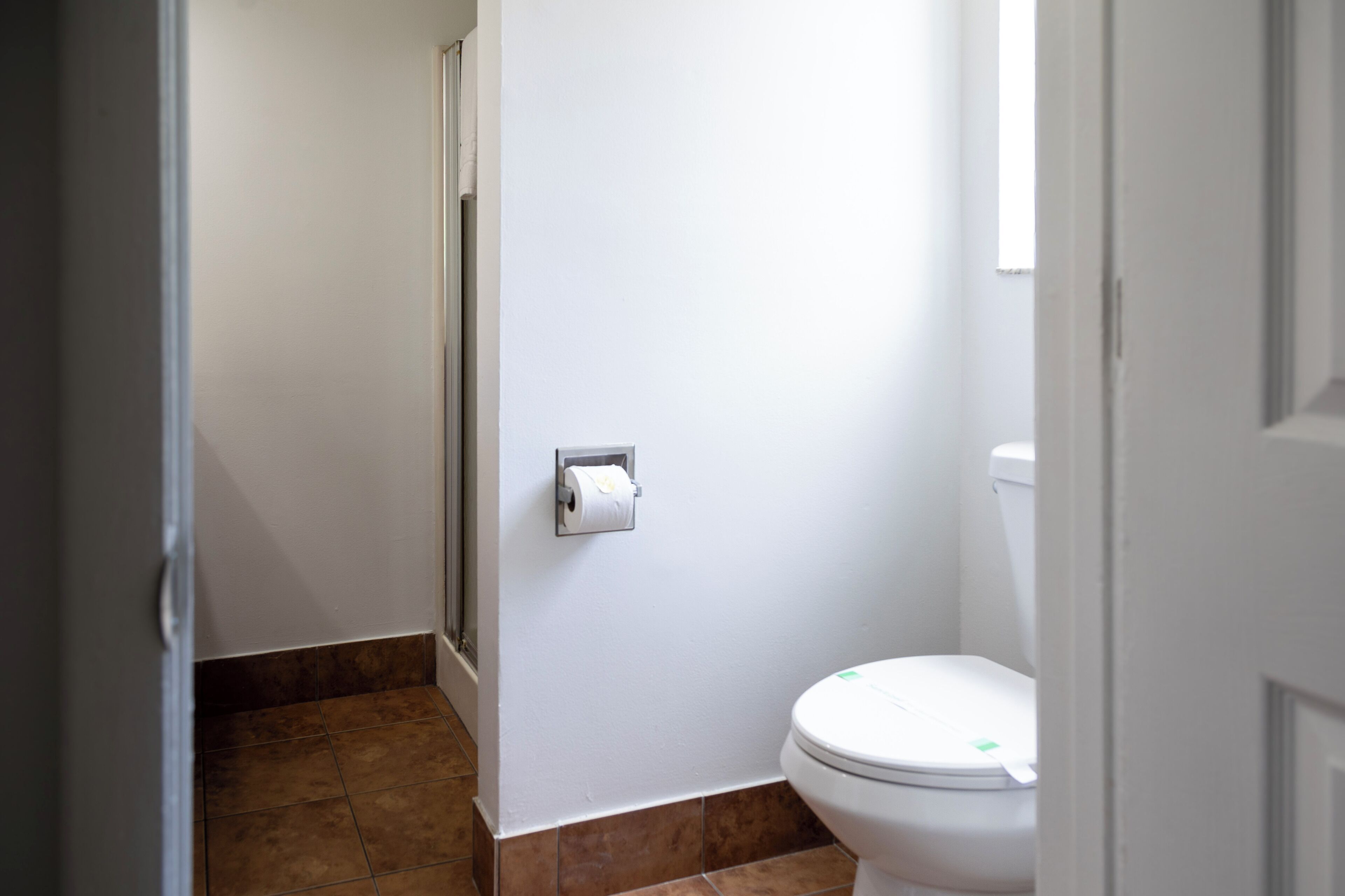 A bathroom with a toilet, a paper towel dispenser, and a shower area.
